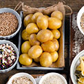 Ein Behälter mit ungeschälten Kartoffeln umgeben von Schüsseln mit Samen und Nüssen