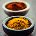 Gelbes Curry Pulver in schwarzer Tonschüssel und dahinter rotes Curry Pulver in heller Tonschüssel