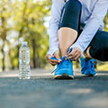 Frau beim Sport bückt sich um die Schuhbänder zu binden eine Wasserflasche steht daneben auf der Straße