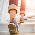 Frau in blauen Sneakers geht gerade weiße Treppen hoch 