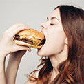 Brünette Frau isst genüsslich und mit geschlossenen Augen einen Burger