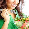 Junge Frau in grüner Bluse ist einen Salat mit einer Gabel aus einer durchsichtigen Schüssel