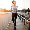 Junge Frau in hellem Top und dunkler Hose mit Flasche in der Hand joggt entlang einer Straße