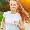 Frau mit weißem T-Shirt joggt lachend mit Kopfhörern