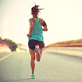 Frau in blauem Top und schwarzer kurzer Trainingshose von hinten die eine lange leere Straßen entlang joggt