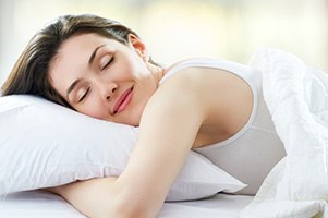 Frau die sich gemüglich im Bett in ihr weißes Kissen kuschelt Frau die sich gemüglich im Bett in ihr weißes Kissen kuschelt
