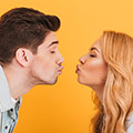 Frau und Mann küssen sich fast mit gespitzen Lippen vor orangem Hintergrund