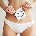 Frau in weißem Slip hält einen Zettel mit einem Smiley vor ihren Bauch