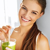 Frau in weißem Top hält ein Smoothieglas in der Hand und lächelt Frau in weißem Top hält ein Smoothieglas in der Hand und lächelt