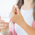 Frau hält eine weiße Tablette und ein Wasserglas in der Hand