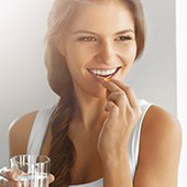 Frau in weißem Top hält ein Glas in der Hand und nimmt mit der anderen eine Tablette Frau in weißem Top hält ein Glas in der Hand und nimmt mit der anderen eine Tablette