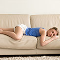 Frau in blauem Oberteil schläft auf einer beigen Couch