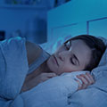 Frau schläft in weiße Bettwäsche eingehült in einem dunklen Raum