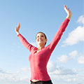 Frau in einem pinken Oberteil streckt die Arme in Richtung des blauen Himmels und lacht