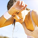 Frau beim Sport unter freiem Himmel wischt sich mit weißem Schweißband Schweiß von der Stirn