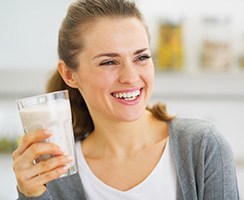 Frau lacht und hält ein großes Glas mit einer milchigen Flüssigkeit in der Hand