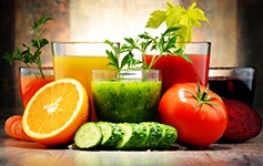 Fünf Gläser mit bunten Obst- und Gemüsesäften und Obst und Gemüse davor auf einem Tisch
