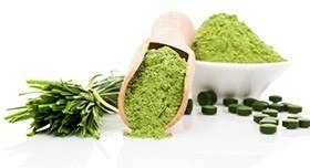 Grünes Pulver in einer Schale und einer Schaufel, daneben grüne Tabletten und Chlorella Stiele