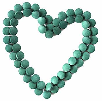 Grünes Herz gelegt aus Chlorella Tabletten auf weißem Hintergrund Grünes Herz gelegt aus Chlorella Tabletten auf weißem Hintergrund