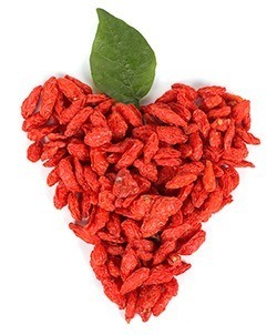 Ein aus Goji Beeren geformtes Herz mit Blatt auf weißem Hintergrund