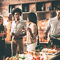 Frauen und Männer auf einer Party stehen vor dem Buffet mit kleinen Happen
