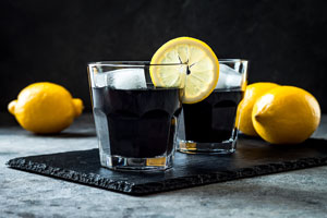Zwei gläser mit schwarzen Getränken, einer Zitronenscheibe und ganzen Zitronen