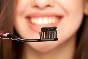 Schwarze Zahncreme auf einer Zahnbürste mit einer lächelnden Frau im Hintergrund
