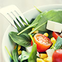Schüssel mit grünem Salat und Tomaten in weißer Schüssel mit Gabel