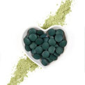 Spirulina Tabletten in einer herzförmigen kleinen Schale auf einem Streifen Spirulina Pulver