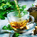 In durchsichtige Teetasse auf durchsichtigem Untersetzer von Blättern umgeben wird goldgelber Tee eingegossen