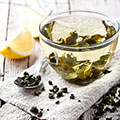 Durchsichtige Teetasse mit grünem Tee und Teeblättern gefüllt mit Zitrone und Teelöffel daneben liegend