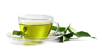 Durchsichtige Teetasse mit grünem Tee gefüllt und Teeblättern auf weißem Hintergrund