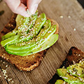 Zwei Toasts mit Avocado belegt und Samen bestreut auf hölzernem Untergrund