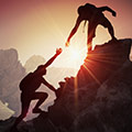 Zwei Bergsteiger reichen sich die Hand während dem Aufstieg mit Sonnenuntergang im Hintergrund